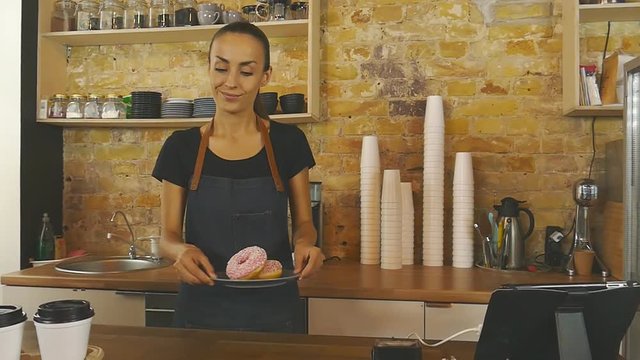 Smiling waitress giving cup of coffee and donats to the customer.
