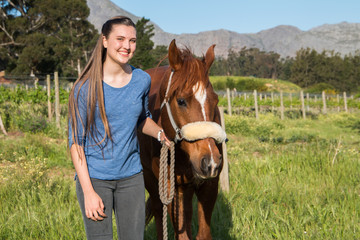 Teenage girl standing with her chestnut Arab horse looking at the camera smiling with countryside...