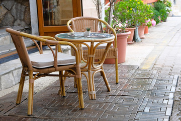 Rattan table and chairs in outdoor summer veranda of coffee house. Flower pots with green plants in background.