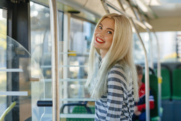 Young blond happy woman student in strip t-shirt with red lips standing in city bus or trolleybus....