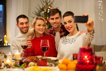 holidays and celebration concept - happy friends taking selfie by smartphone at home christmas dinner
