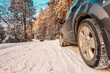 Luxury black crossover made a stop on the winter road in the forest. SUV. Car tires on winter road covered with snow. Vehicle on snowy alley in the morning at snowfall.