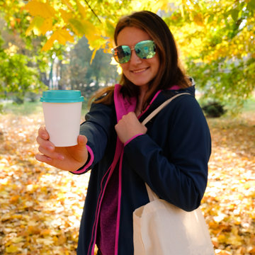 Happy young woman holding a paper cup with coffee
