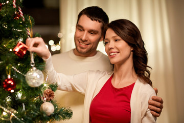 winter holidays and people concept - happy couple decorating christmas tree at home