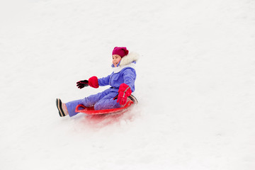Fototapeta na wymiar childhood, sledging and season concept - happy little girl sliding down on snow saucer sled outdoors in winter