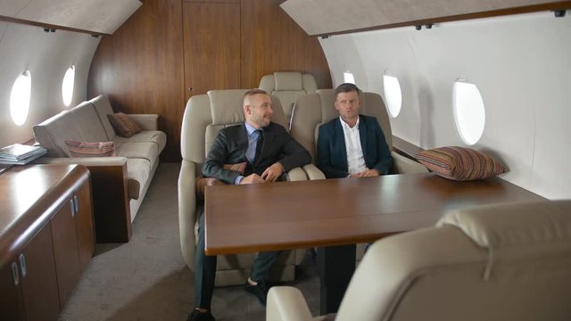 Two businessmen talking, sitting in airplane interior during flight. modern business private airliner. Wide shot