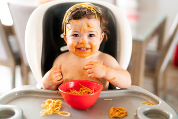 child girl, eating spaghetti for lunch and making a mess at home in kitchen
