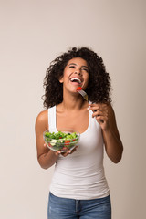Laughing woman eating healthy salad over light background