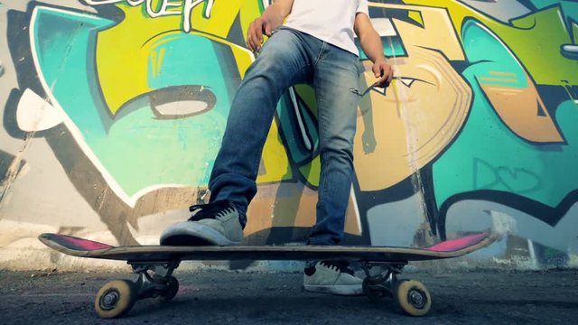 One man rolls a skateboard with a leg while resting. Slow motion.