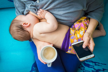Mom and baby having breakfast. Breastfeeding, coffee and smartphone