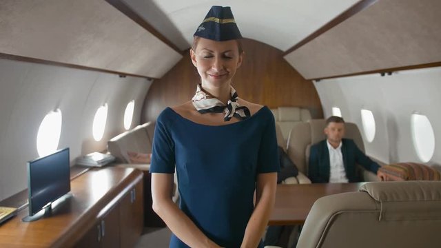 Stewardess smiling and applause to camera inside of luxury private business jet cabin. Business Passengers sitting on background