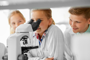 education, science and children concept - kids or students with microscope studying biology at school laboratory