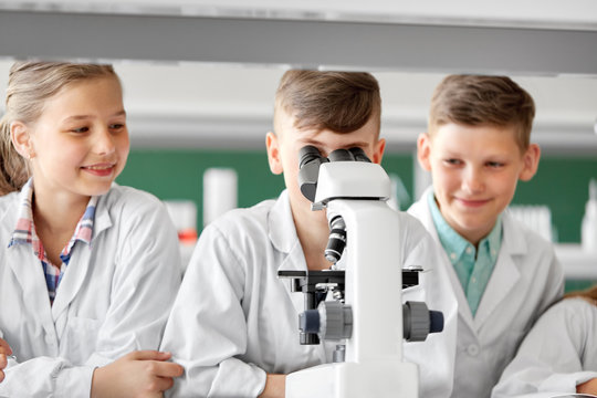 education, science and children concept - kids or students with microscope studying biology at school laboratory