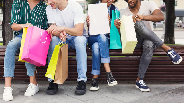 Friends sitting on bench and looking in shopping bags