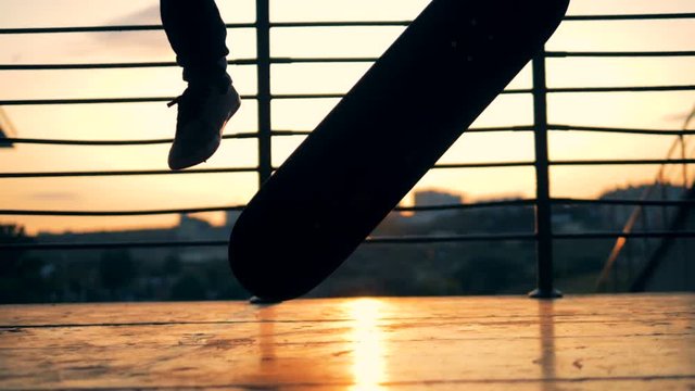 Skater fails doing trick. Person jumping on a skateboard on a sunset background, slow motion.