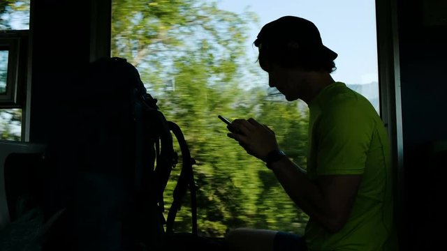 Man tourist uses a smartphone while sitting in a train on the background of a beautiful mountain landscape and hills