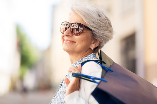 sale, consumerism and people concept - senior woman in sunglasses with shopping bags in city