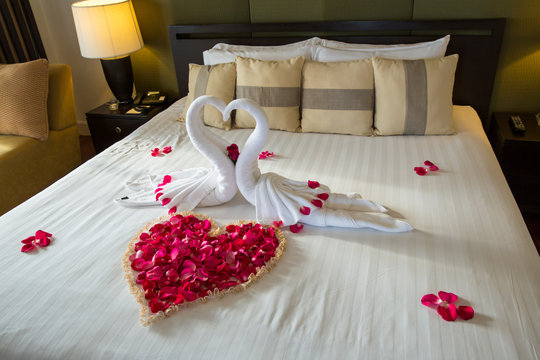 two swans made from towels are kissing on honeymoon white bed. creamy  pillow and heart form, valentine signature made from red rose flower on bed  decoration in bedroom.Valentine background.honey moon Stock Photo