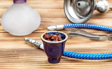 Hookah bowl with flavour tobacco and parts of hookah on wooden table.