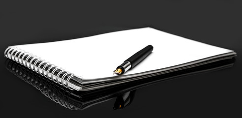 Notepad with pen on black reflective background.