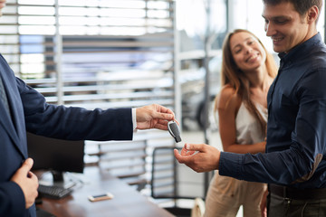 Unrecognizable male consultant giving car key to buyers after successful deal in auto show, close...