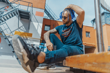 Young attractive man with blue dreadlocks touching his hair.