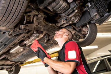 handsome mechanic based on car in auto repair shop with tablet on hand