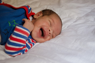 two weeks old newborn baby boy smilin while sleeping on white quilt