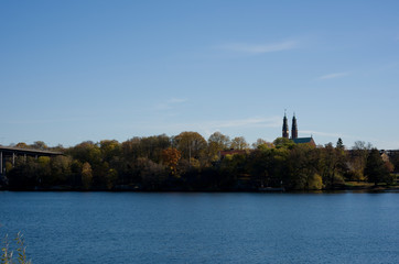 Obraz premium Stockholm water front with landmarks, boats an autumn day with blu sky and sea, orange and red leafs.