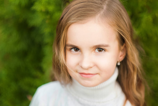 Portrait of a beautiful little girl close-up in a white sweater on a background of green textural natural background