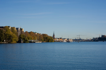 Fototapeta premium Stockholm water front with landmarks, boats an autumn day with blu sky and sea, orange and red leafs.