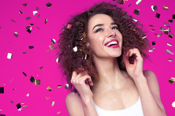 Beautiful smiling young woman on pink background with flying confetti