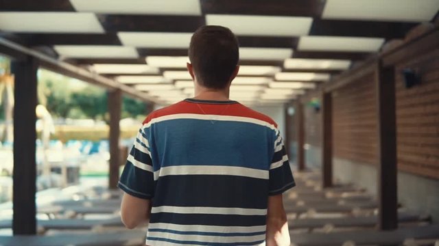 View from behind of a casual guy by the pool looking for lounge chair to lie. Man traveling in summer, tourist abroad in a resort, vacation.