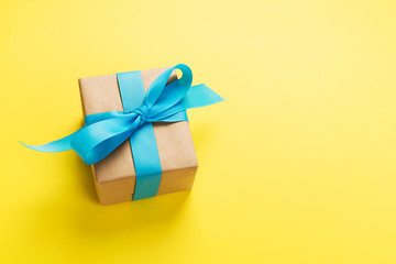 gift wrapped and decorated with blue bow on yellow background with copy space. Flat lay, top view