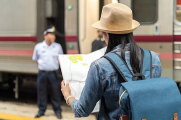 An backpack journalist lady holding map going to asking direction and assistance from a train police in railway train station in Bangkok.