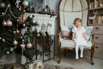 little happy girl sits in an armchair and waits for gifts for the holiday of Christmas and New Year