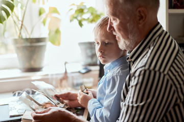 senior man and little boy holding and looking at family photo album in living room