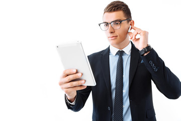 Business man in glasses and suit, wireless headphones, holding a tablet and using it in the Studio...