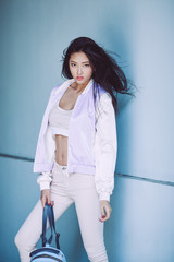 Woman Trendy Fashion. Attractive sporty asian girl in full length with elegant hairstyle and perfect soft colorful makeup. Female with perfect slim body in sport trendy clothes against fancy wall on