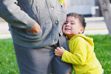 Shy smiling latin boy holding his mom.