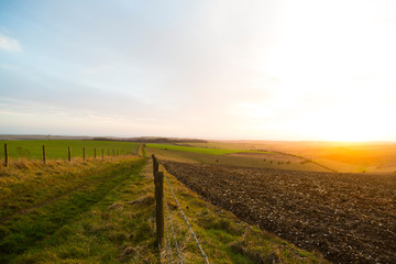Ditchling Beacon, Sussex, UK. A fence and mud track lead towards the horizon while the sun sets behind the rolling fields of Sussex.
