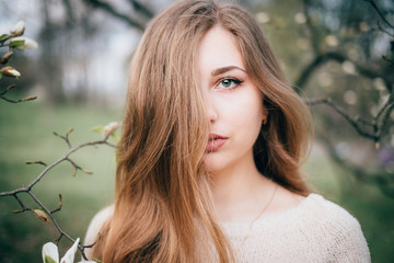 Naklejka premium Portrait of beautiful plus size young woman posing in spring blossoming magnolia garden, creative film-like toning