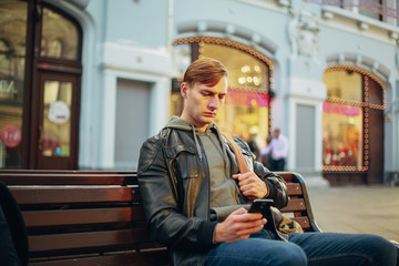 Brutal man sits on a bench and is boring using a smartphone