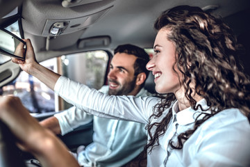 Beautiful couple is looking at rearview mirror and smiling while sitting in their new car