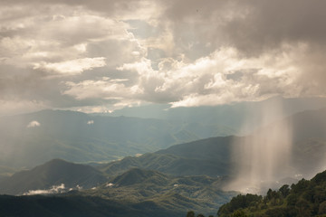 Sun shining beam beautifully through the dense rain cloud with mountain.