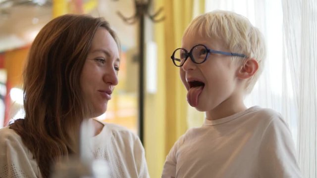 Mom and her son are waiting for an order in a cafe. The boy dabbles and shows language. Mom explains to her son that it is impossible to do so. They are cute hugging. The family is wearing white sweat