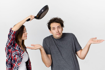 Young couple arguing in kitchen. Frustrated wife with cooking pan screaming to her husband