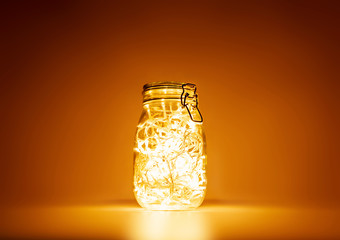 Glass jar with yellow light garland inside, holiday mood