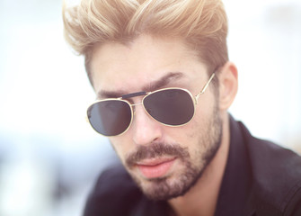 A stylish bearded male sits and uses a smartphone.