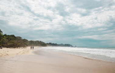 Two backpacking travelers walking down the wide white sand of Red Frog Beach, a Caribbean island off the coast of Panama